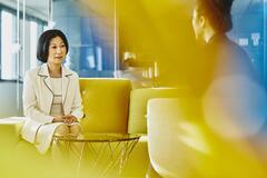 Women in an office talking. Japan. Primary color: yellow.