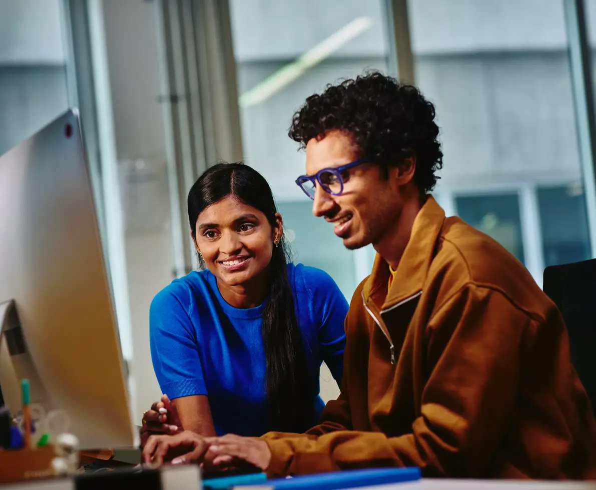 Male with blue glasses and female looking at a computer screen sitting at a desk