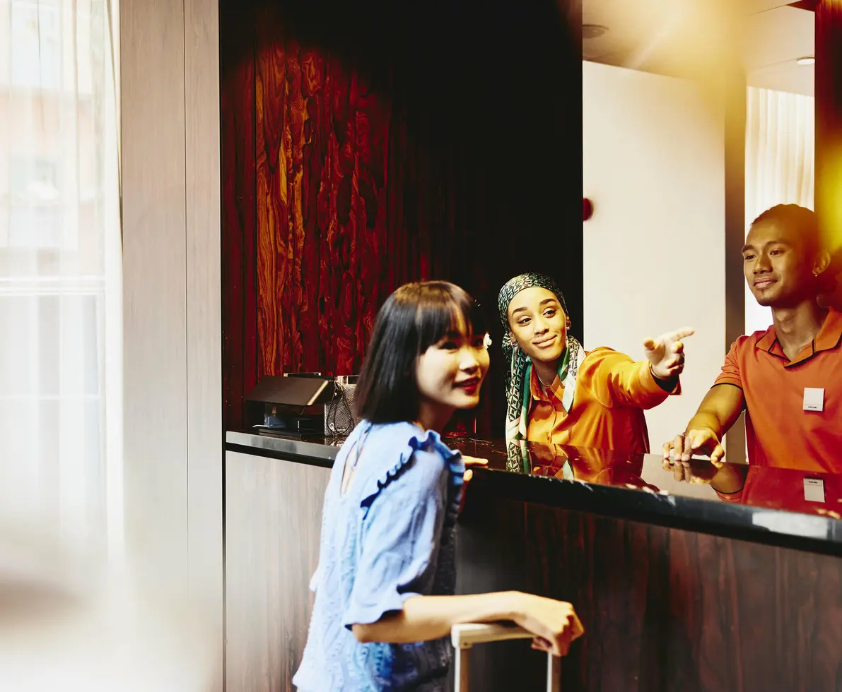 male and female working at a hotel reception desk helping a guest.
