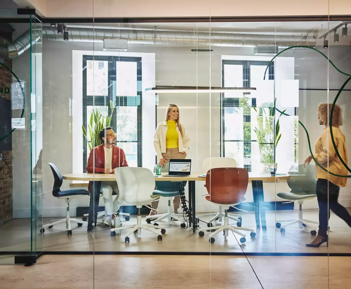 Female and male are sitting and female is standing at a table in a office meeting room