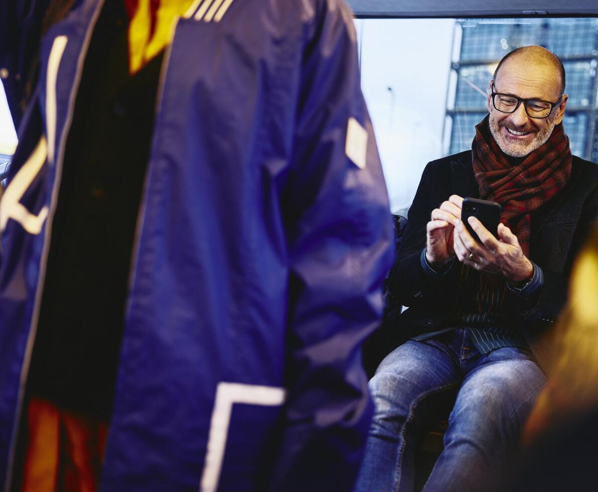 Man sitting in a bus, smiling, looking down at his phone.