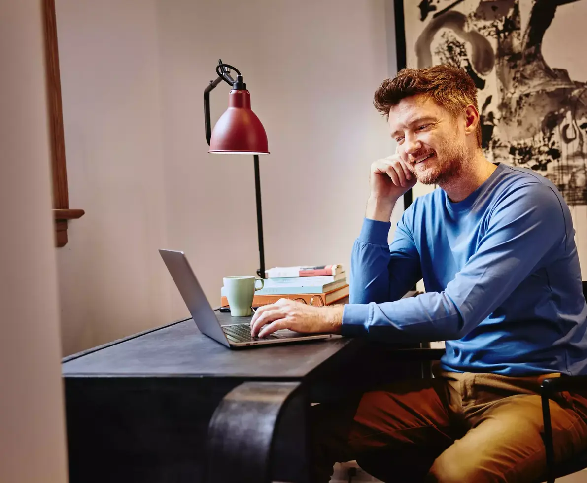 Male in a blue shirt sitting at a desk working on his laptop